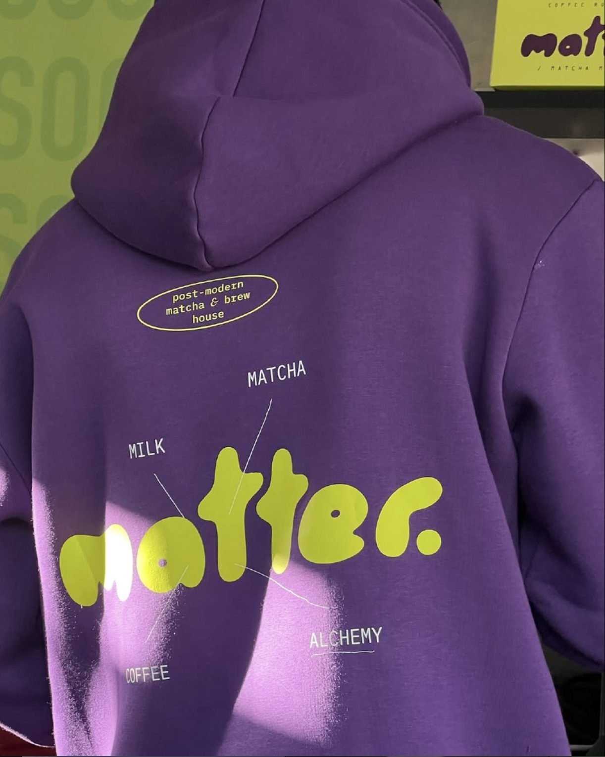 Back of a purple MATTER hoodie with the acid-green blob wordmark and diagram labels reading milk, matcha, coffee and alchemy.